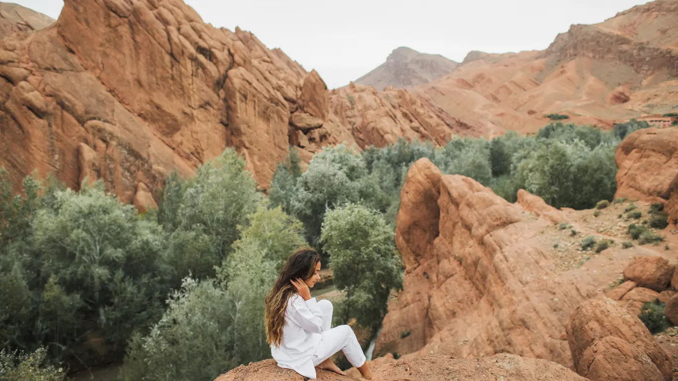 Woman sitting on red rock cliffs overlooking lush valley in Dades Gorge – part of a 4 days desert tour from Marrakech to Merzouga