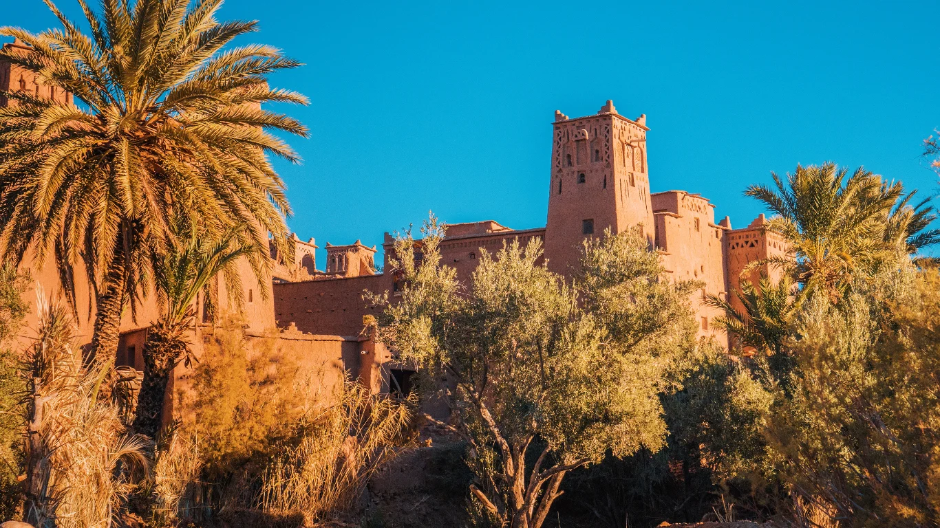 Kasbah Ait Ben Haddou with palm trees under a clear blue sky – a stop on a Marrakech 4 days itinerary