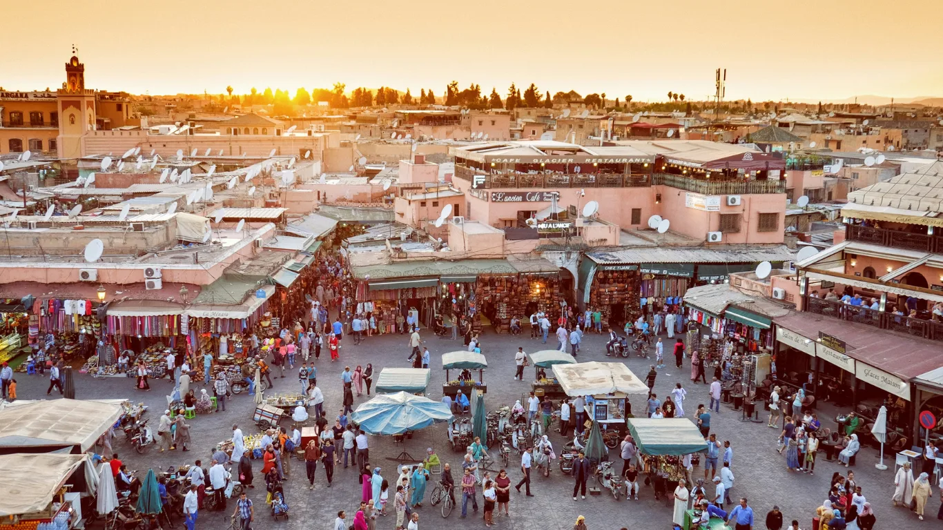 Bustling marketplace in Marrakech at sunset, filled with shops, street vendors, and locals – starting point of a 3-day luxury desert tour to Fes.