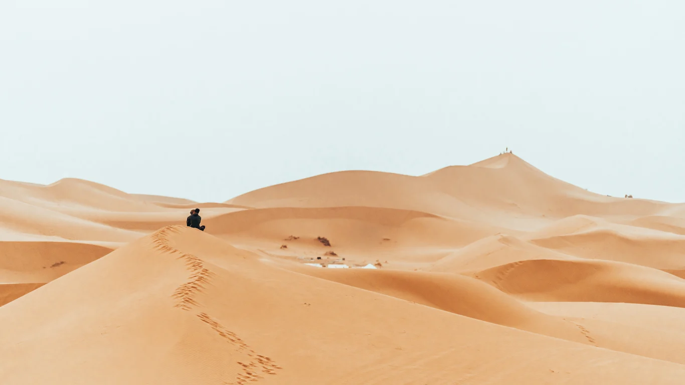A lone traveler sitting on top of a sand dune in the vast Sahara Desert, reflecting the serenity of a Morocco itinerary 10 days experience.