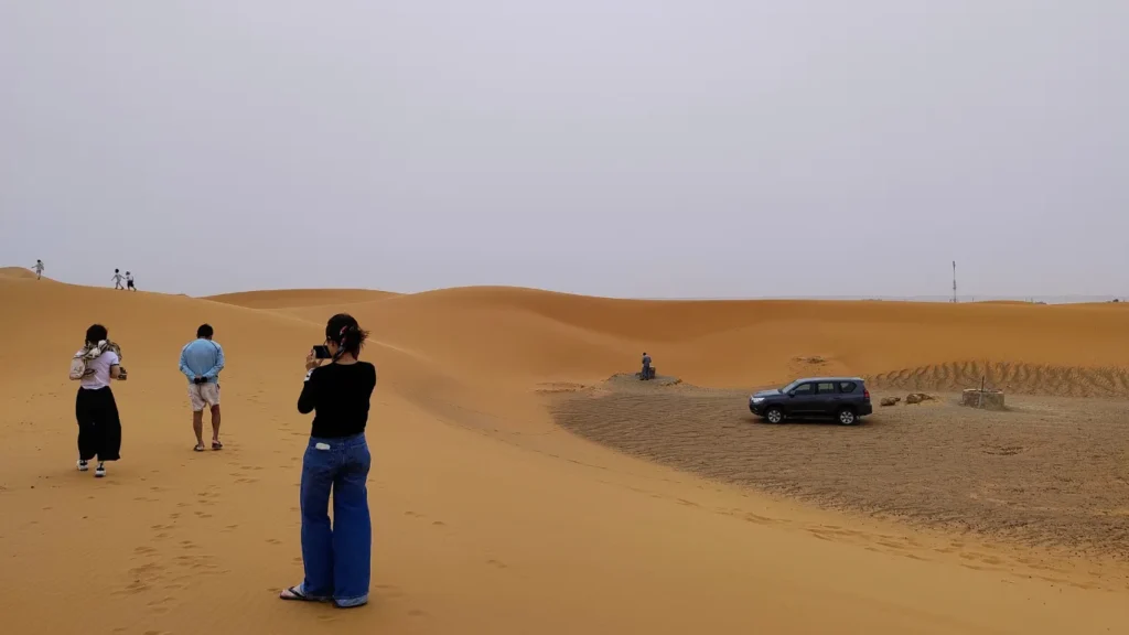 Tourists exploring golden sand dunes during Morocco tours in the Sahara Desert, with a 4x4 vehicle parked nearby.