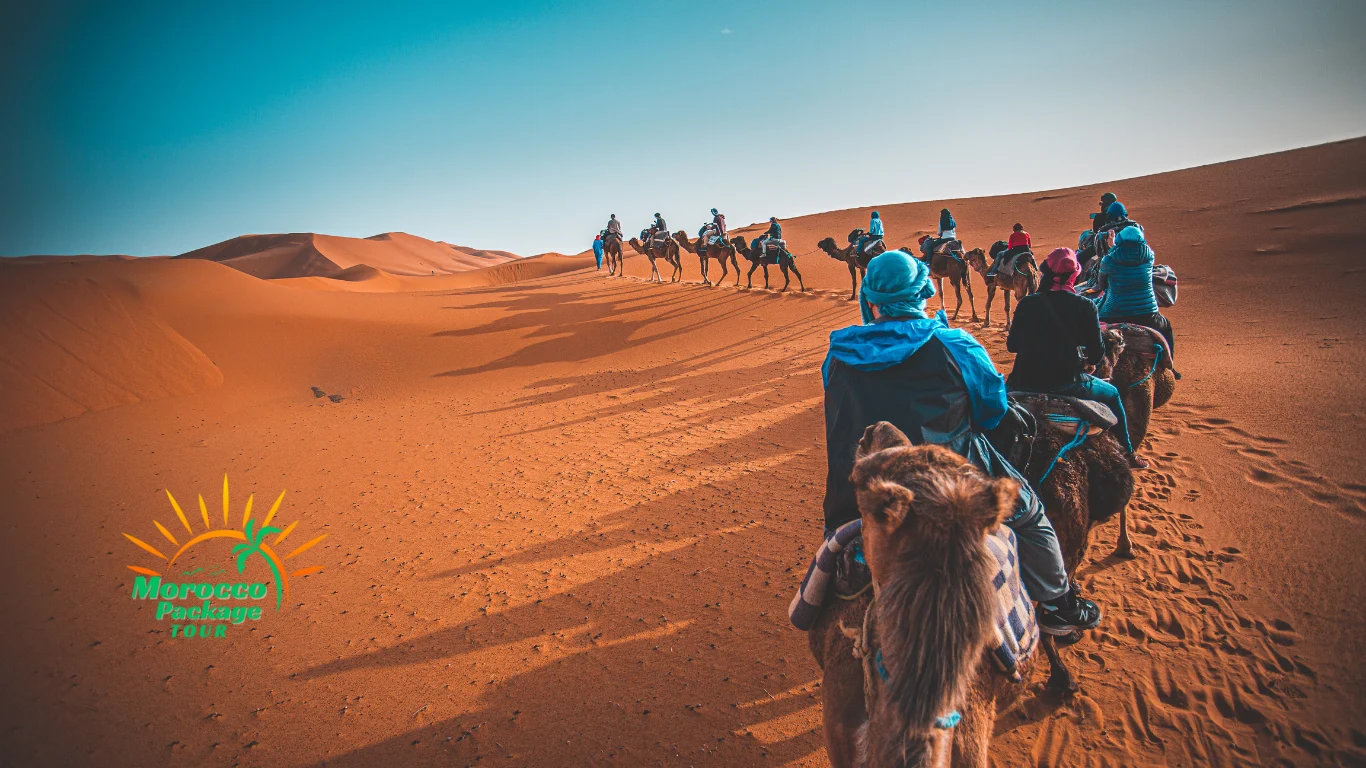 Group of travelers riding camels through the Sahara Desert at sunset — a key highlight of a 12 days tour from Casablanca.