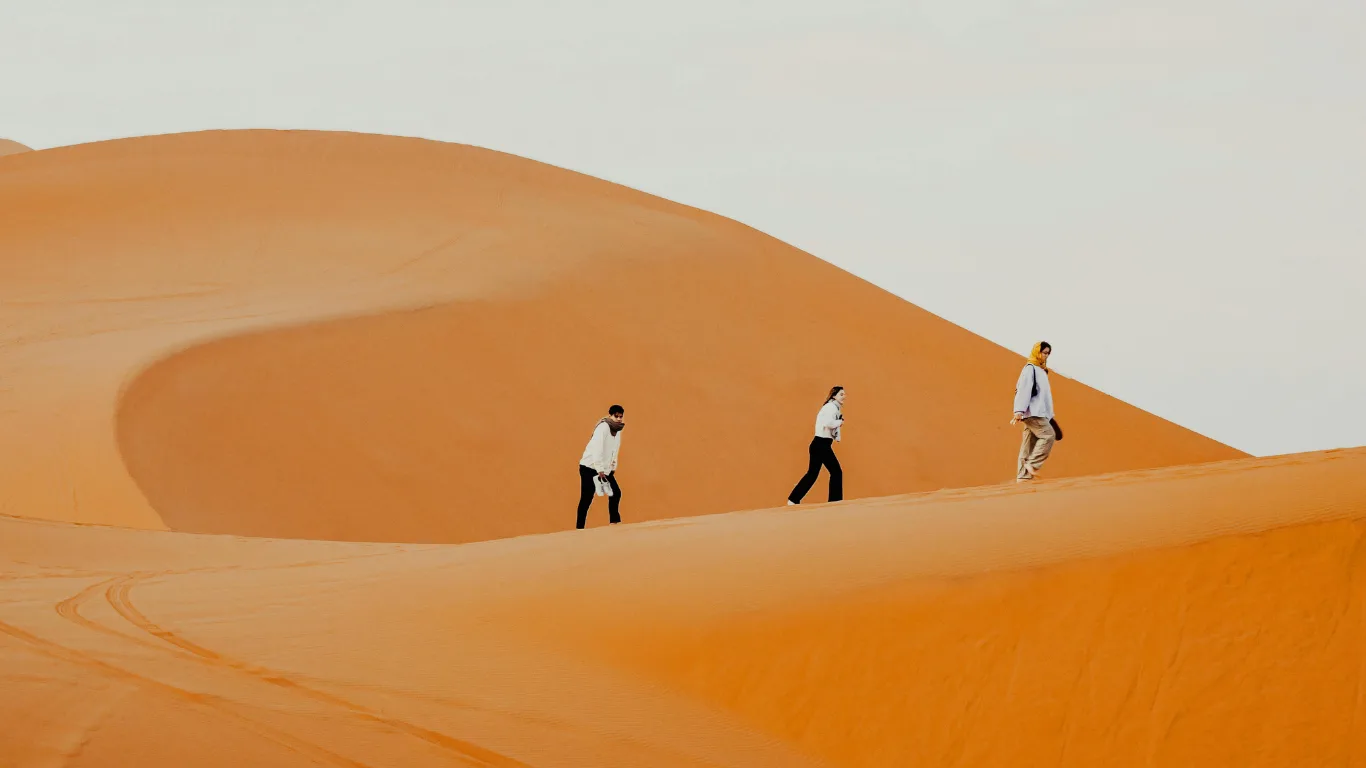 Travelers walking on golden dunes during a 4 days tour from Agadir to Marrakech through the Moroccan desert.