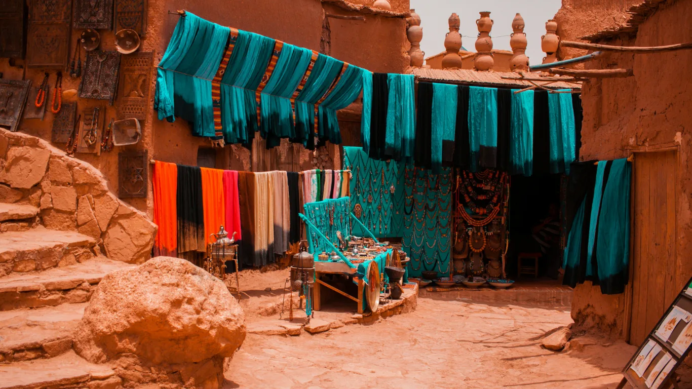 Traditional Moroccan market with colorful fabrics and jewelry during a day trip from Agadir to Marrakech.