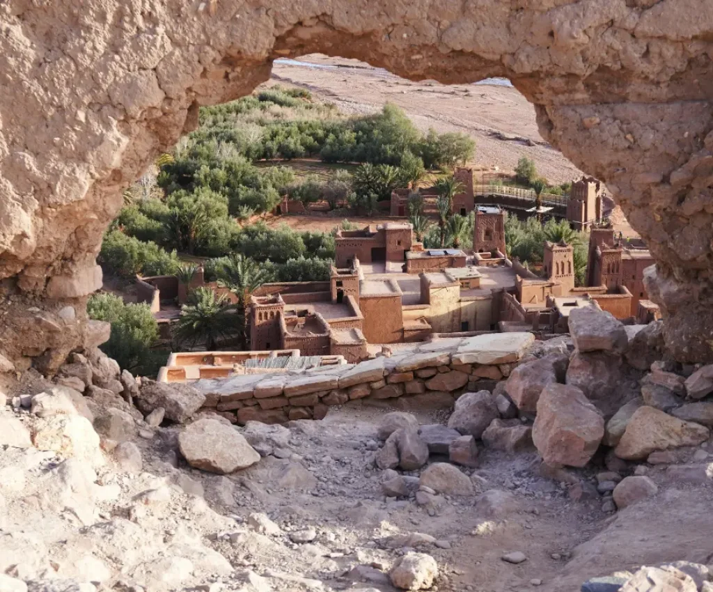 3 Day Tour from Marrakech to Merzouga – Aït Benhaddou Viewpoint Aït Benhaddou seen through a stone archway, showcasing ancient kasbah architecture and lush greenery during a Marrakech to Merzouga tour.
