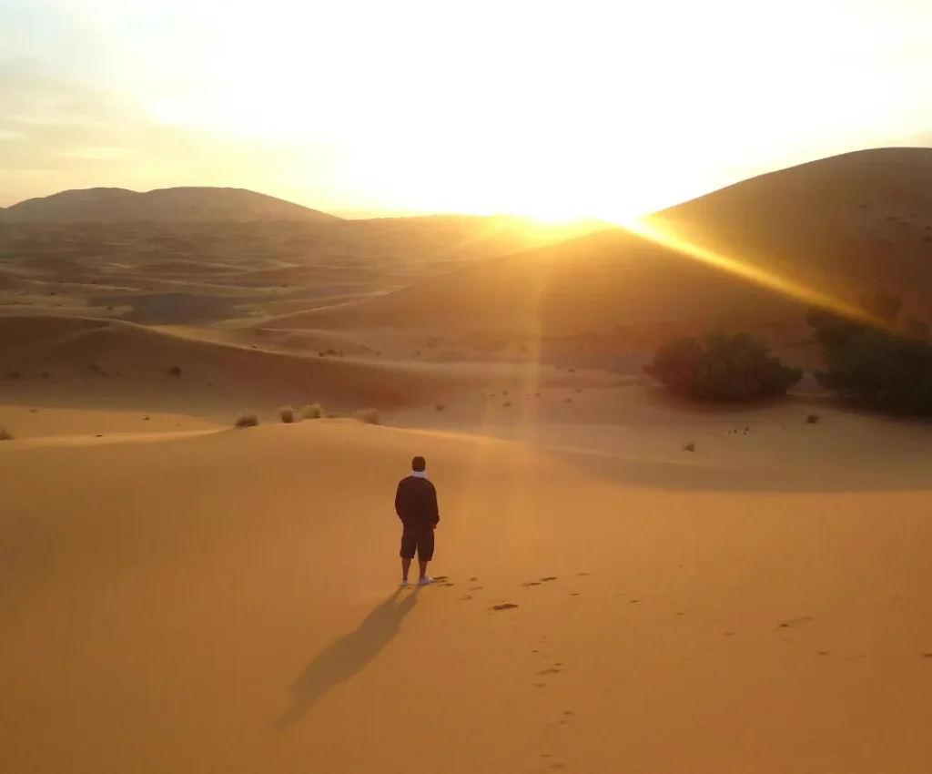 4 Days Tour from Fes to Marrakech – Sunrise in the Sahara Desert Man standing in the golden Sahara dunes at sunrise, part of a 4 Days Tour from Fes to Marrakech.