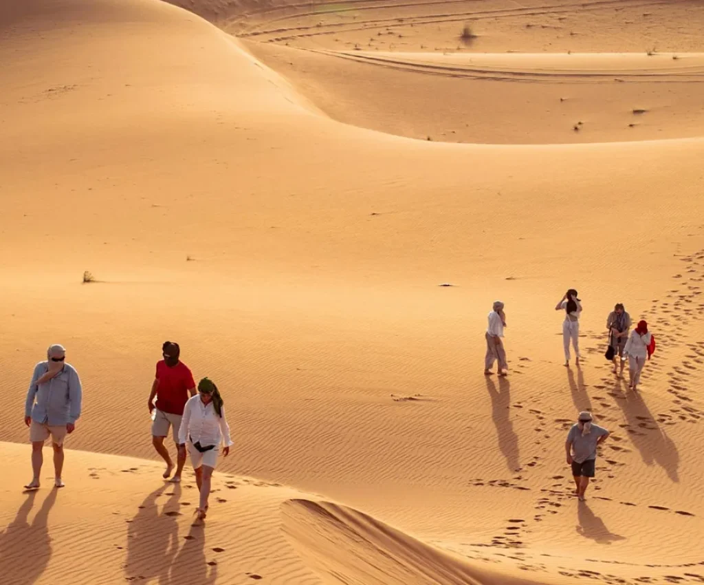 4-Day Morocco Desert Itinerary – Sahara Trekking Adventure Tourists walking across golden sand dunes in the Moroccan Sahara Desert during a 4 day itinerary tour.