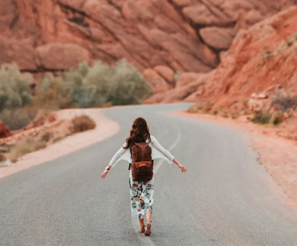 4 Day Trip to Morocco – Mountains, Gorges & Cultural Discovery A woman backpacker walking alone on a winding road through Morocco’s red rock landscape during a 4 day trip to Morocco.