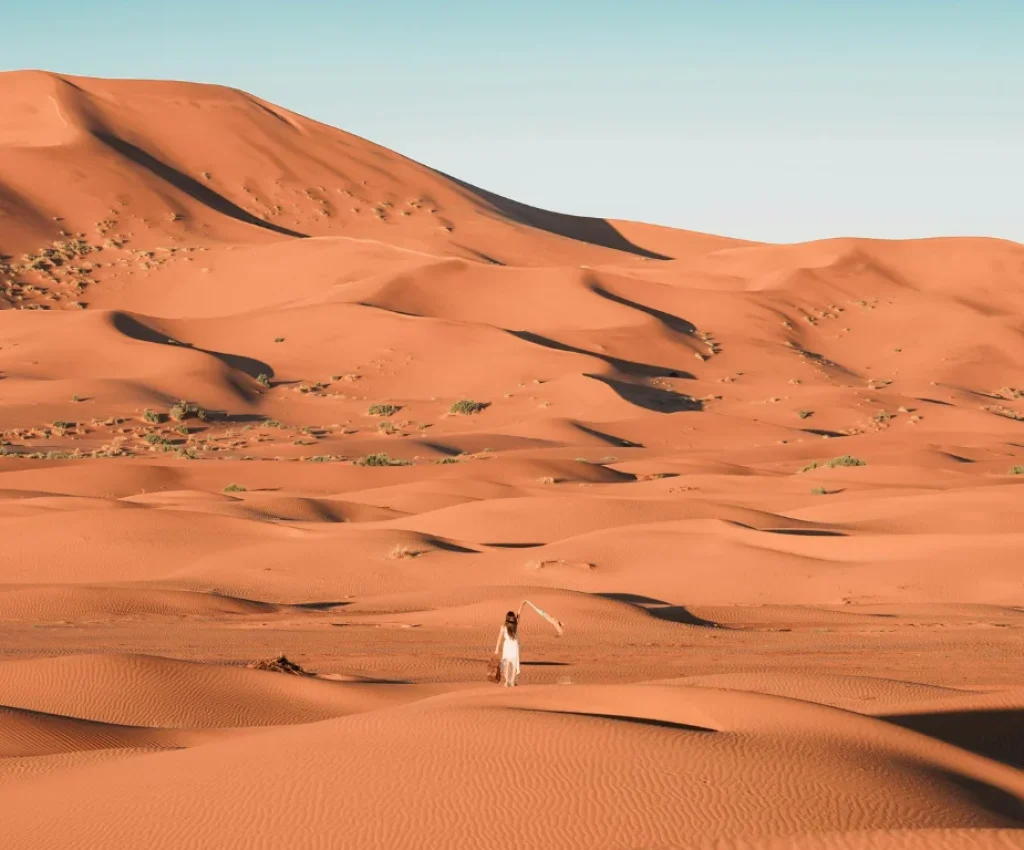 Sahara Desert Adventure on a Fes to Marrakech Tour Woman walking through the golden sand dunes of the Sahara Desert during a Fes to Marrakech tour.
