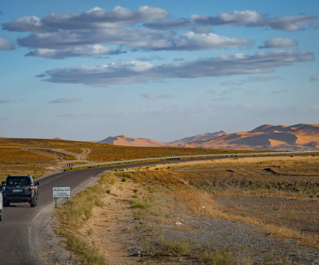 4x4 vehicles driving through a scenic desert road with golden dunes in the distance during a Morocco in 7 days road trip.